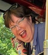 A white woman laughing, holding up a heavily stickered water bottle, sitting in a fire truck.